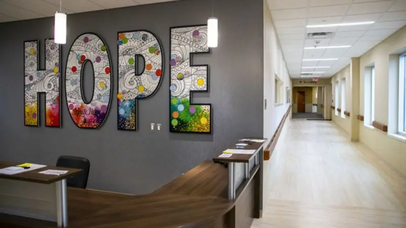 Mostrador de recepción en un vestíbulo limpio y moderno, con grandes cuadros de colores que dicen "ESPERANZA" en una pared gris.