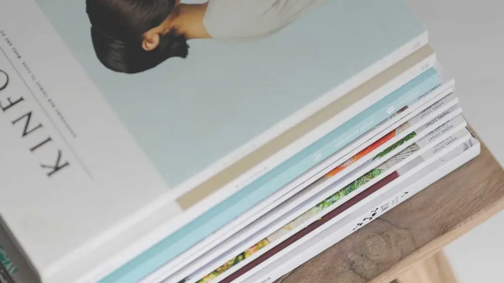 A stack of magazines with colorful covers is placed on a wooden surface, viewed from above at an angle.